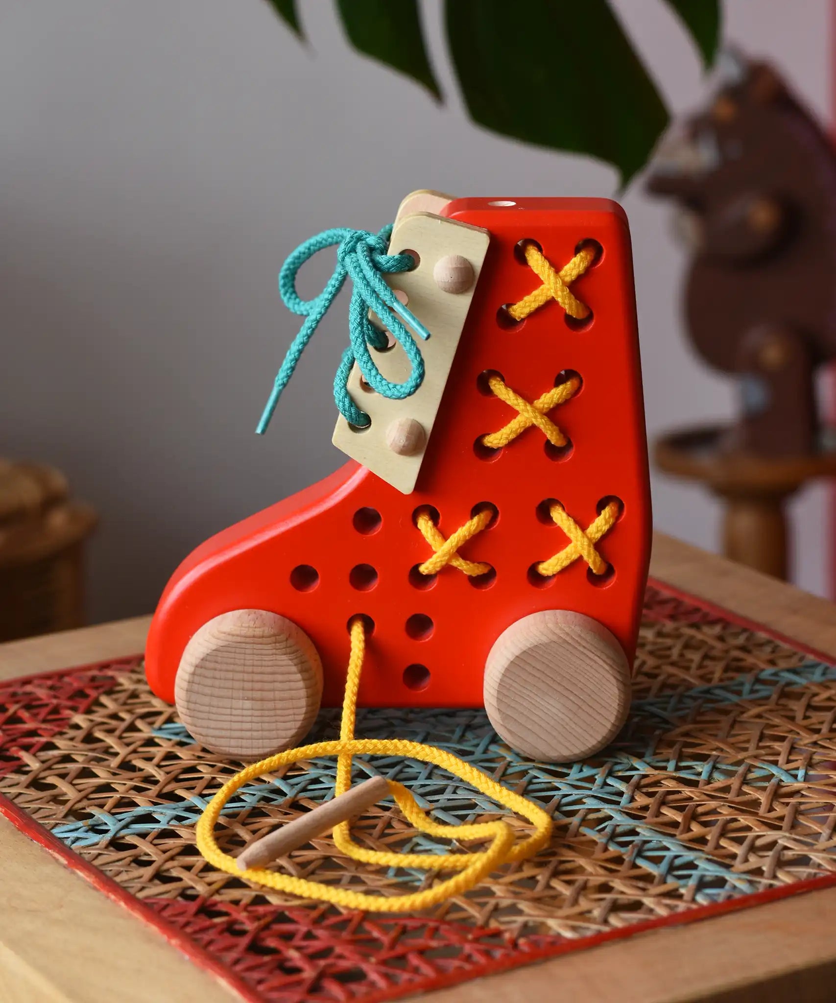 Side of the Bajo red lacing shoe wooden push along toy placed on a rattan stool in the Babipur playroom.