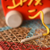 Close up of the wooden thread tip on the Bajo red lacing shoe wooden push along toy.