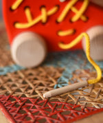 Close up of the wooden thread tip on the Bajo red lacing shoe wooden push along toy.