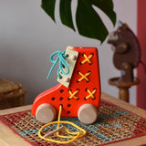 Side of the Bajo red lacing shoe wooden push along toy placed on a rattan stool in the Babipur playroom.