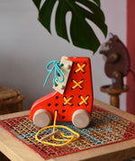 Side of the Bajo red lacing shoe wooden push along toy placed on a rattan stool in the Babipur playroom.