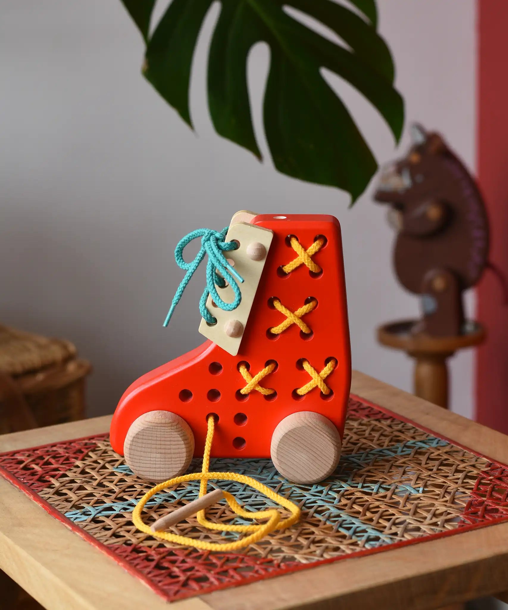Side of the Bajo red lacing shoe wooden push along toy placed on a rattan stool in the Babipur playroom.