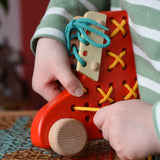 Child playing with the Bajo red lacing shoe wooden push along toy placed on a rattan stool in the Babipur playroom.