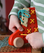 Child playing with the Bajo red lacing shoe wooden push along toy placed on a rattan stool in the Babipur playroom.