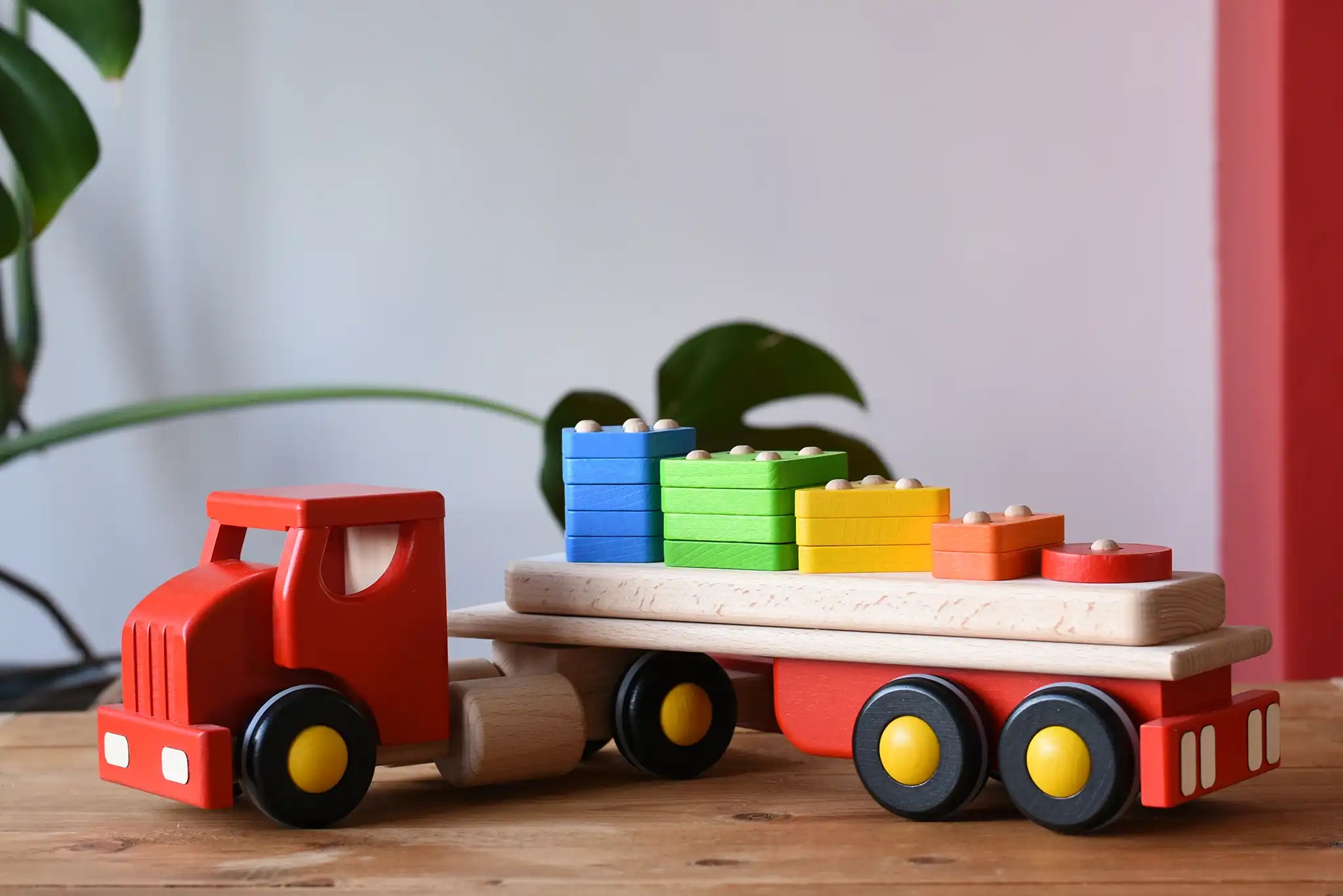Bajo large red cargo truck and wooden shape sorter toy placed on a wooden surface.