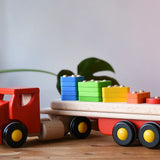 Bajo large red cargo truck and wooden shape sorter toy placed on a wooden surface.