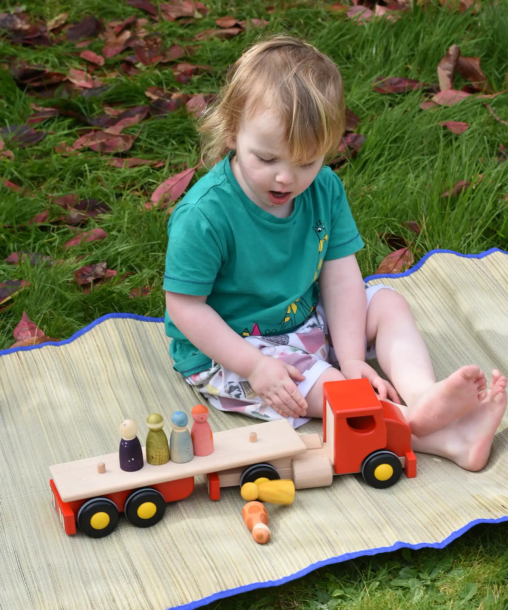 A child playing with the Bajo large red cargo truck and wooden shape sorter toy placing Grapat Wild Crew peg dolls on the back. 