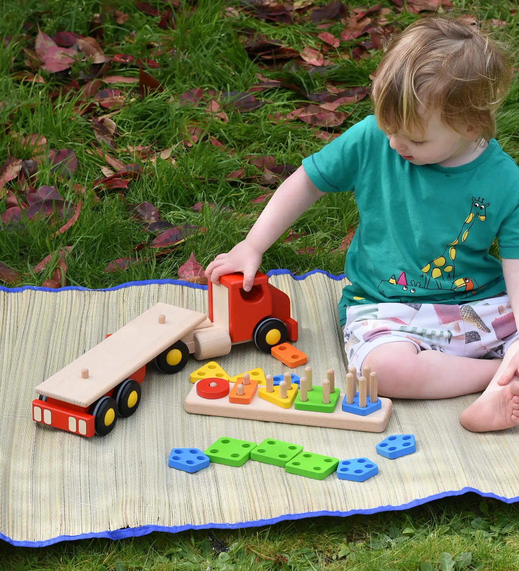 Child playing with the Bajo large red cargo truck and wooden shape sorter toy outdoors. The stacker has been taken off the back of the lorry.