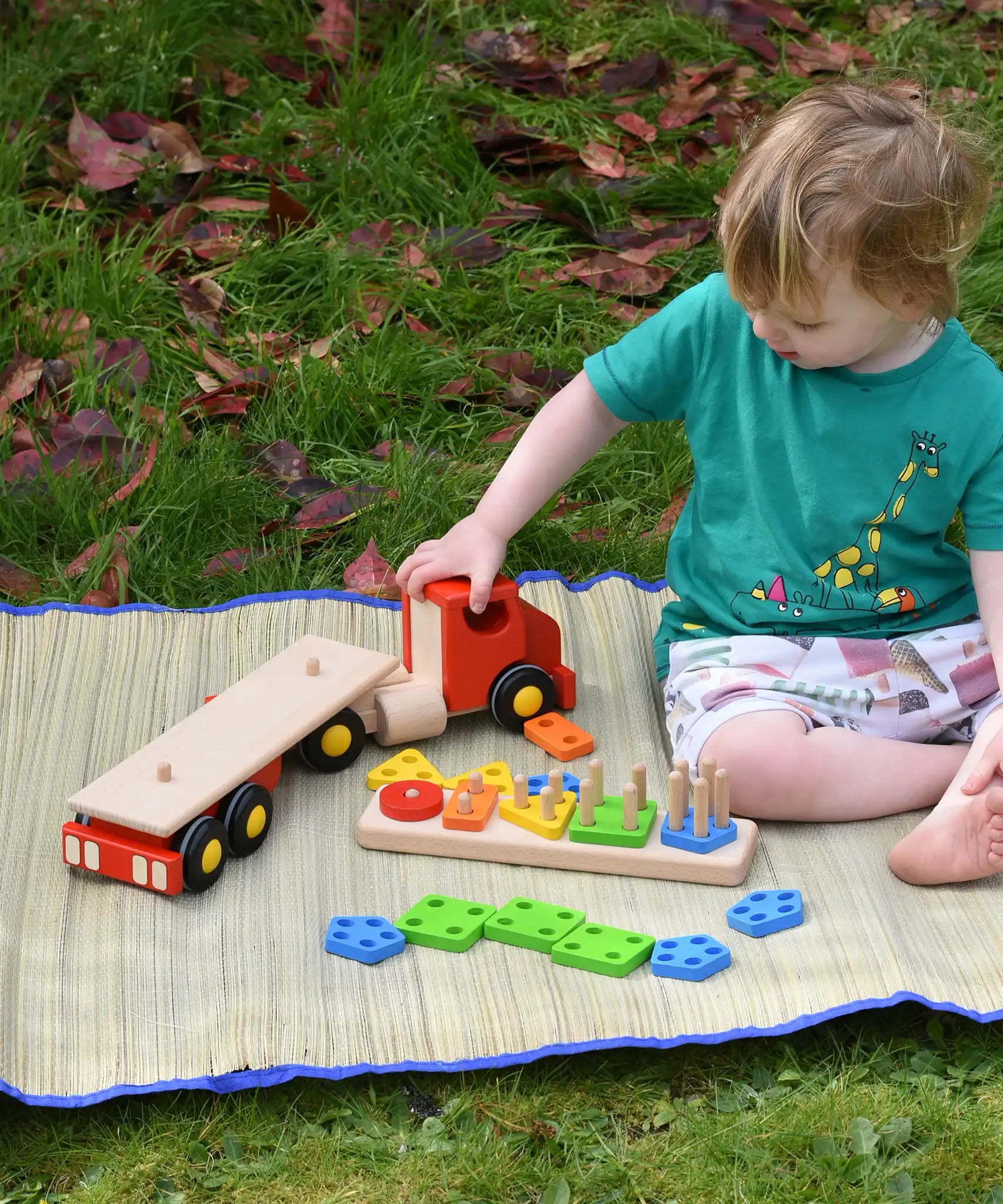 Child playing with the Bajo large red cargo truck and wooden shape sorter toy outdoors. The stacker has been taken off the back of the lorry.