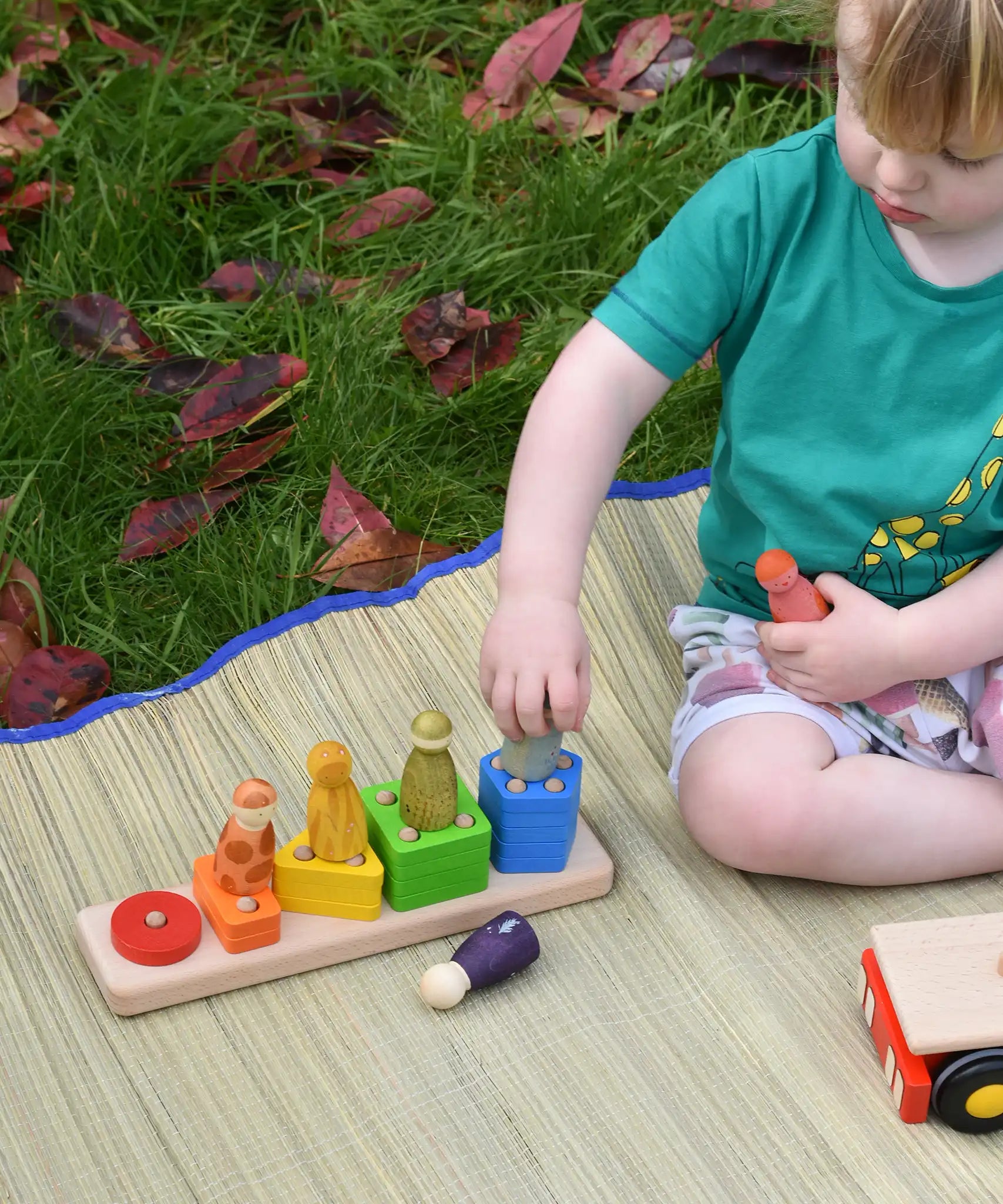 Child playing with the shape sorter from the Bajo large red cargo truck, placing Grapat wooden wild crew peg dolls on the corresponding colours. 