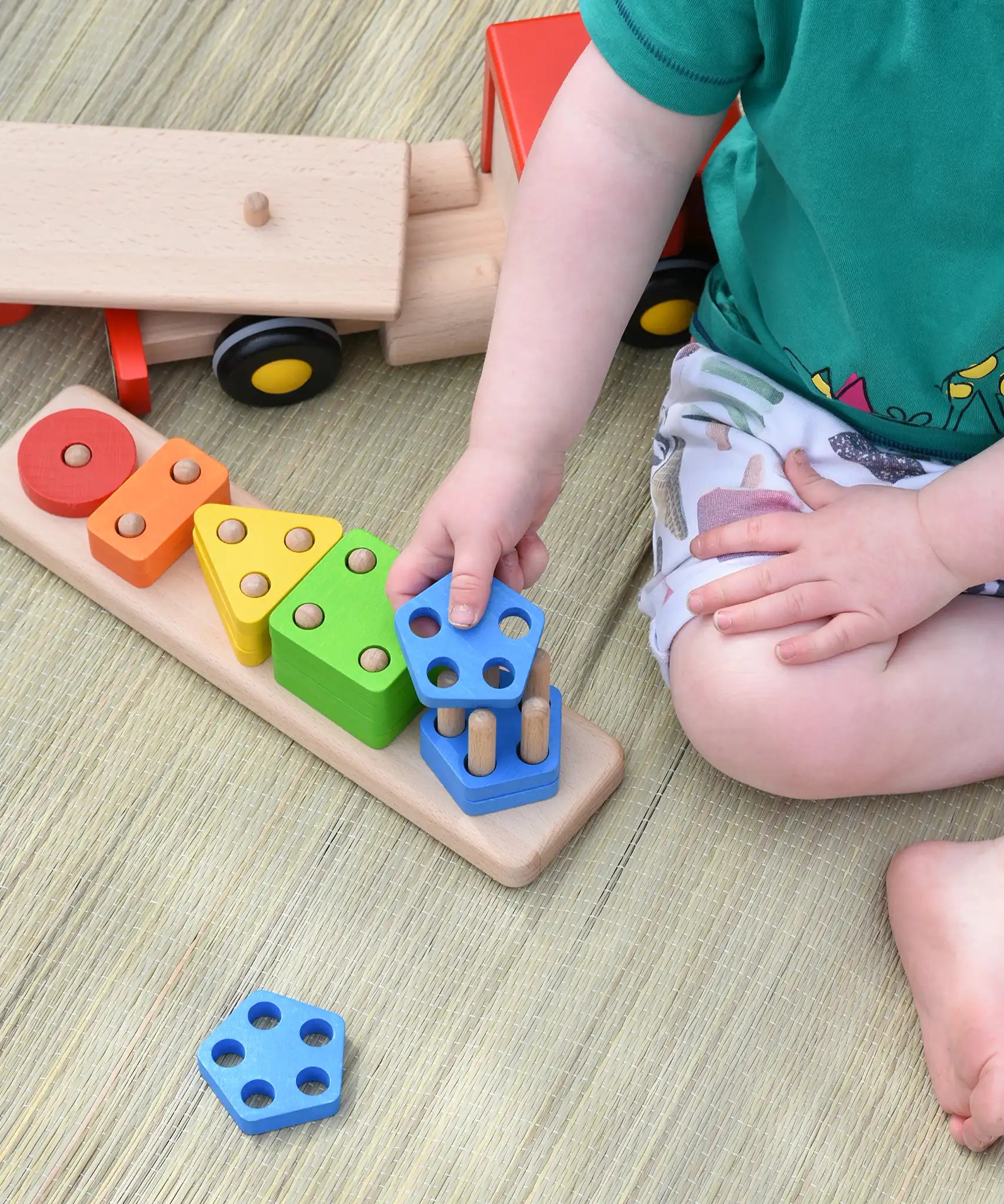 Close up of child placing a wooden shape on the Bajo large red cargo truck and wooden shape sorter toy base.