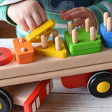 Close up of child placing a yellow triangle on the base of the Bajo large red cargo truck and wooden shape sorter toy.