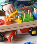 Close up of child placing a yellow triangle on the base of the Bajo large red cargo truck and wooden shape sorter toy.