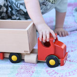 Child pulling the Bajo large truck and trailer wooden toy along by holding the red cab.