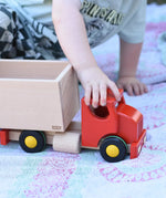 Child pulling the Bajo large truck and trailer wooden toy along by holding the red cab.