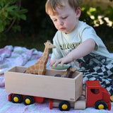 Child playing with the Bajo large truck and trailer wooden toy, placing Bajo pebbles inside with Holztiger animal figures. 