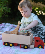 Child playing with the Bajo large truck and trailer wooden toy, placing Bajo pebbles inside with Holztiger animal figures. 