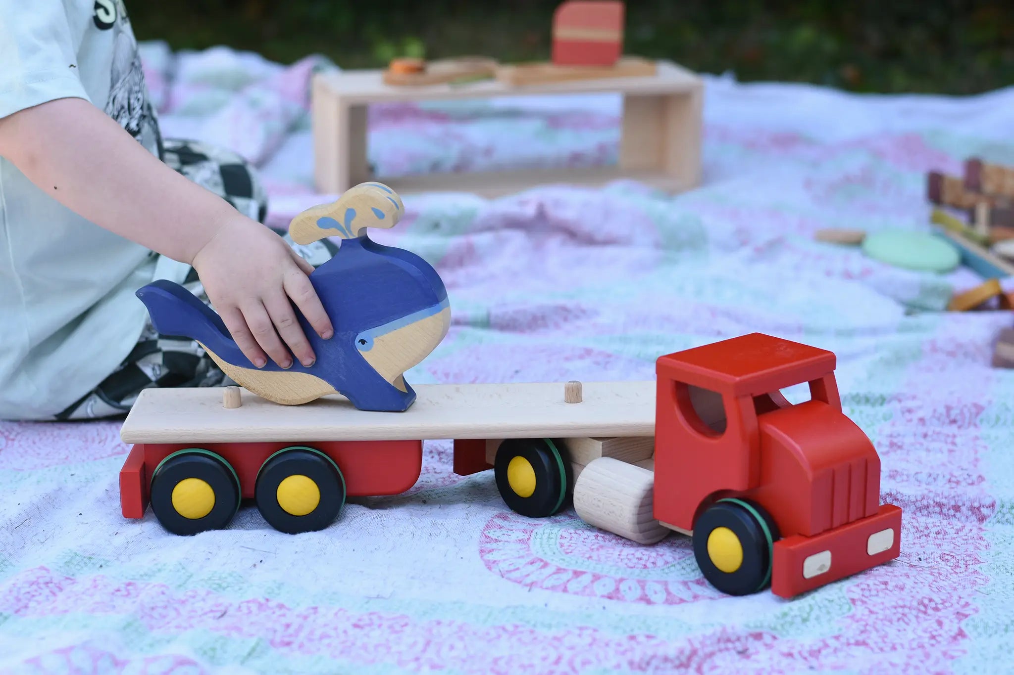 Child placing a Holztiger whale on the back of the Bajo large truck and trailer wooden toy with the trailer box removed. 