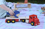 Child placing a Holztiger whale on the back of the Bajo large truck and trailer wooden toy with the trailer box removed. 