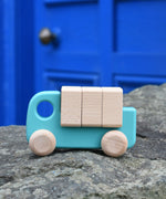 A light blue coloured Bajo truck with blocks placed on a stone wall. This wooden truck is part of a wide range of Bajo wooden toy vehicles available at Babipur.