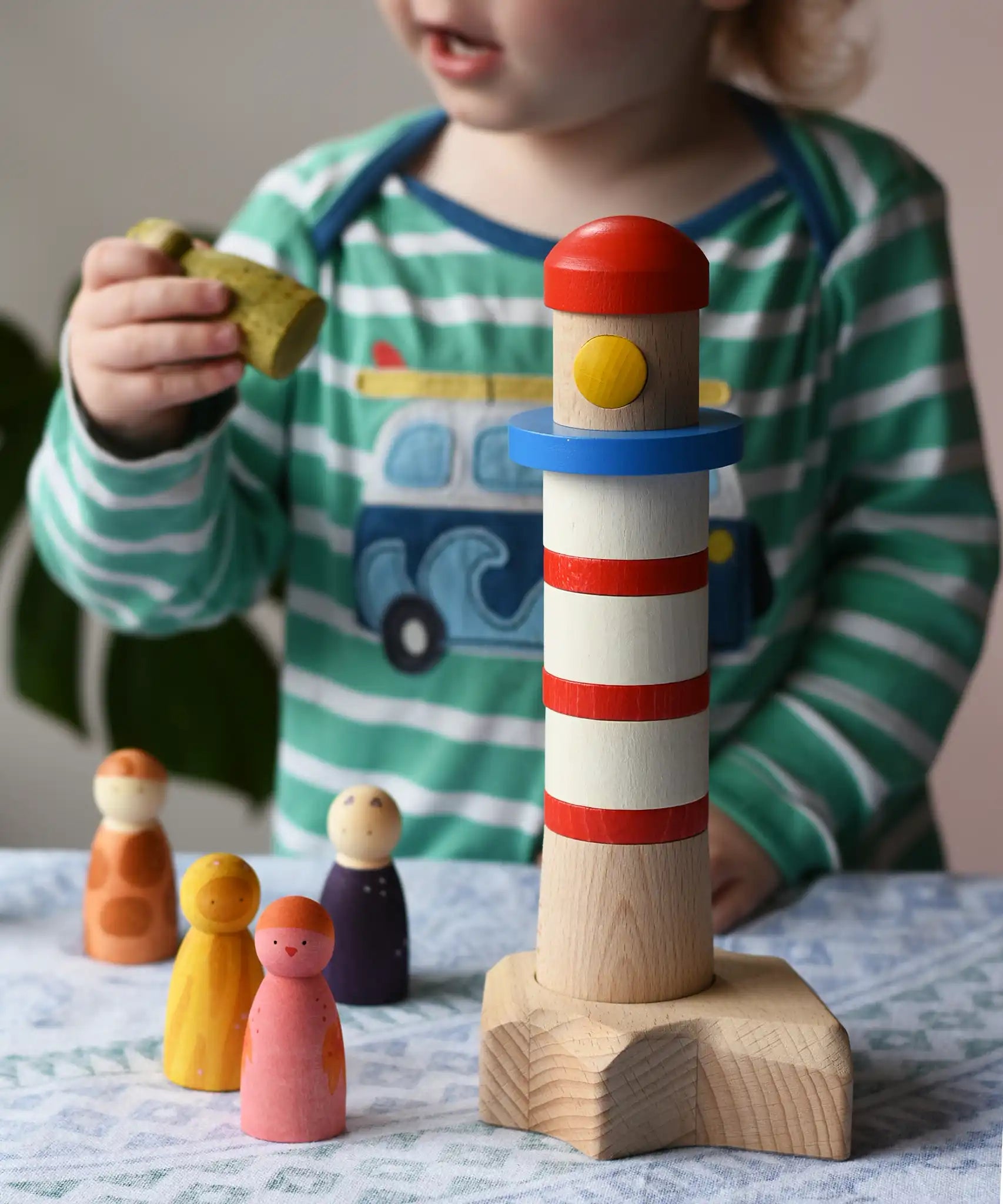 A child p[laying with the Bajo Lighthouse Stacker and Grapat Wild Crew wooden Nin peg dolls.