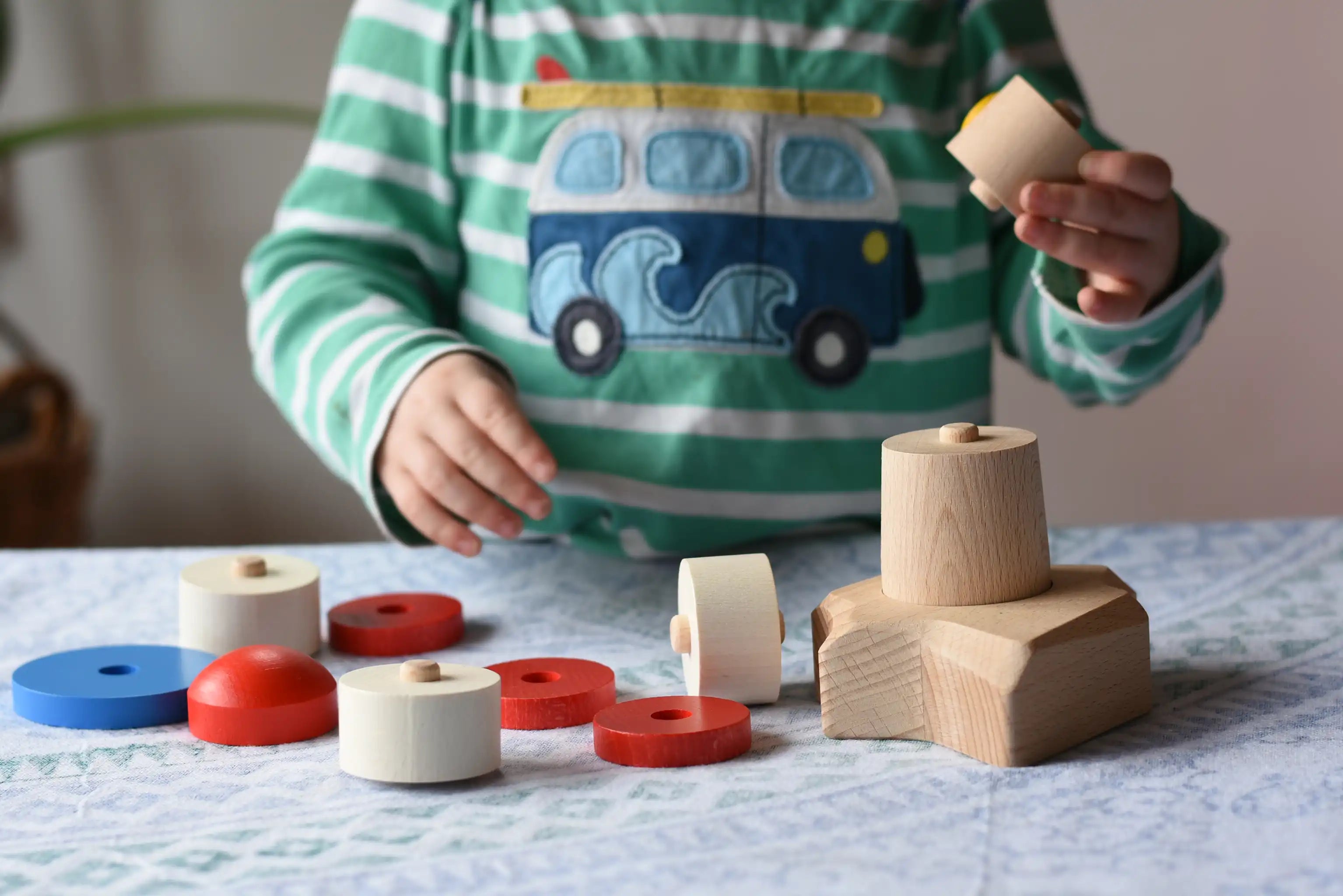 A child starting to assemble the Bajo Lighthouse Stacker all the pieces have been placed on a table.