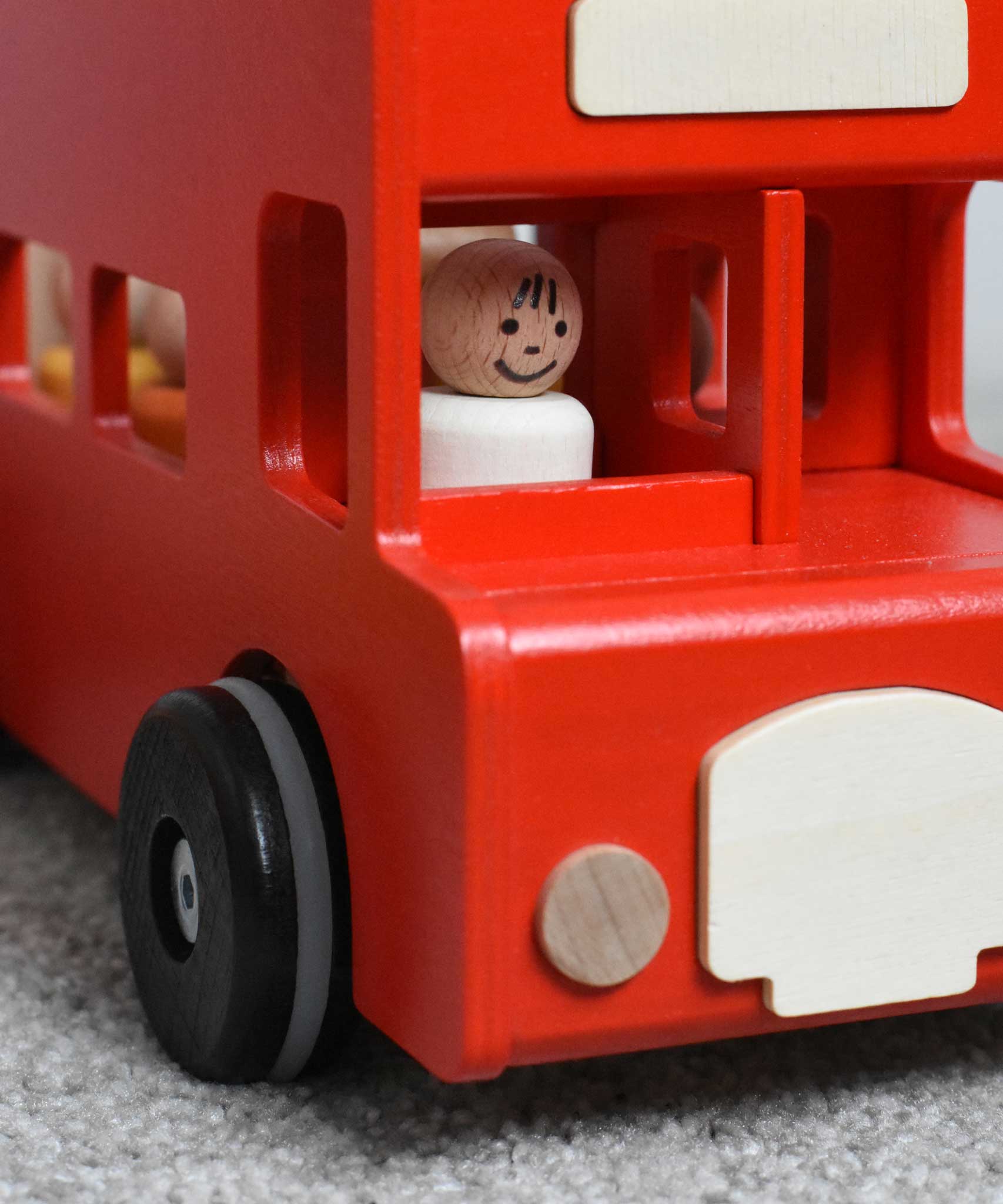 A close up of the  bus driver peg doll from the Bajo London bus wooden toy sitting in the driver's spot on the bus.  These heirloom quality toys by Bajo are part of a wide range of wooden toys available here at Babipur.