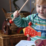 Bajo magnetic fishing game toy. Child holding wooden rod with red fish attached.