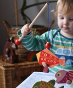 Bajo magnetic fishing game toy. Child holding wooden rod with red fish attached.