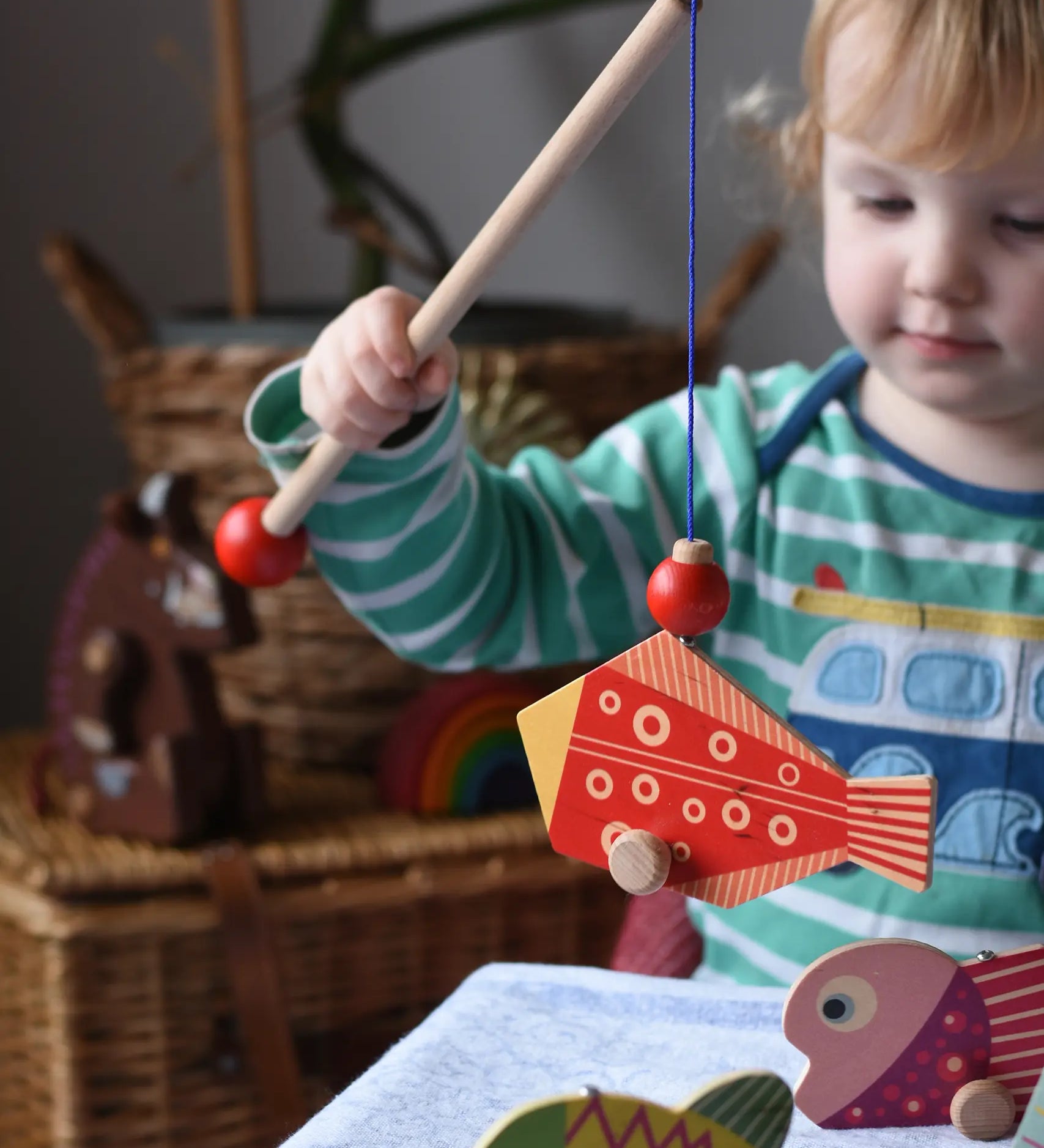 Bajo magnetic fishing game toy. Child holding wooden rod with red fish attached.