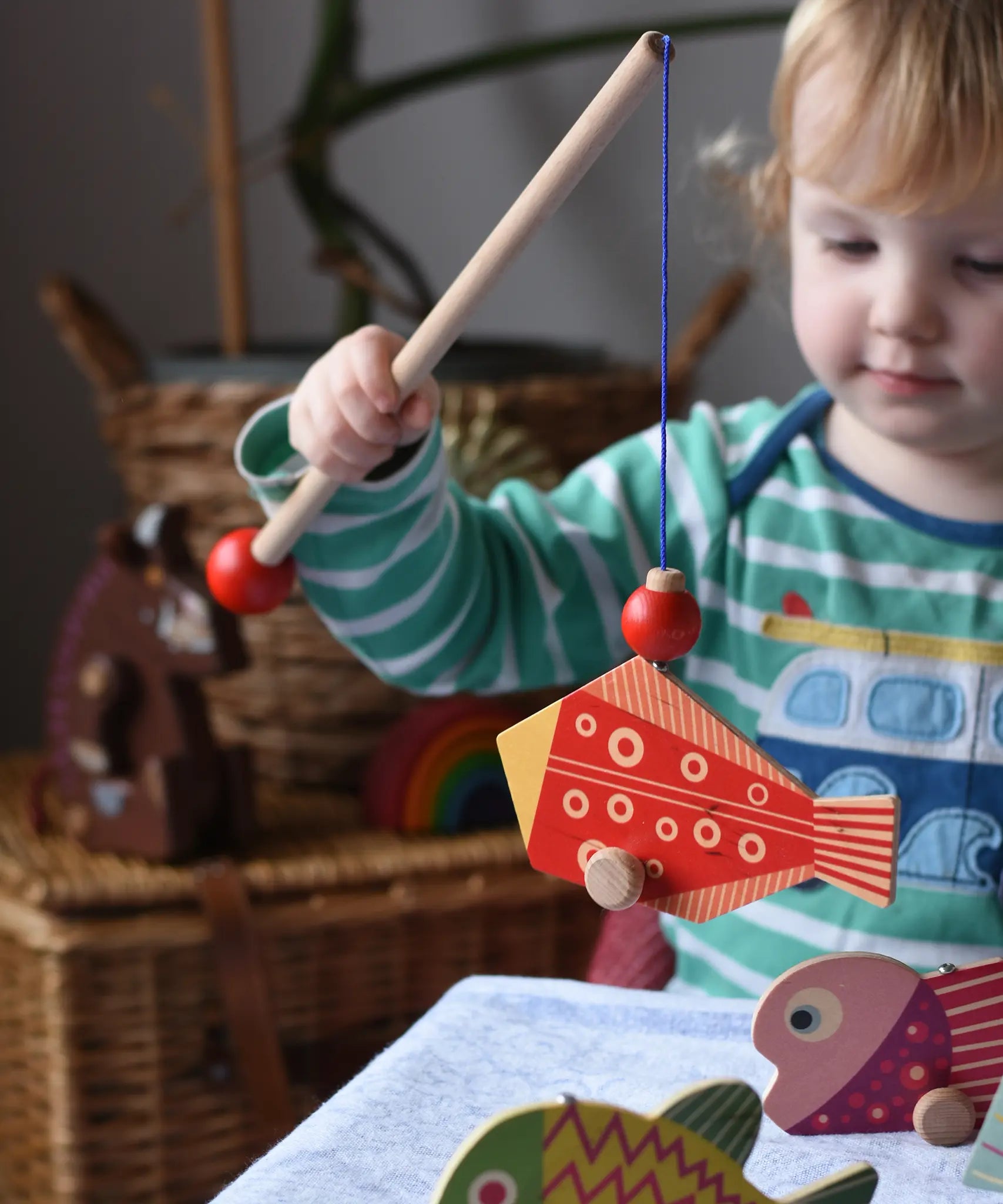 Bajo magnetic fishing game toy. Child holding wooden rod with red fish attached.