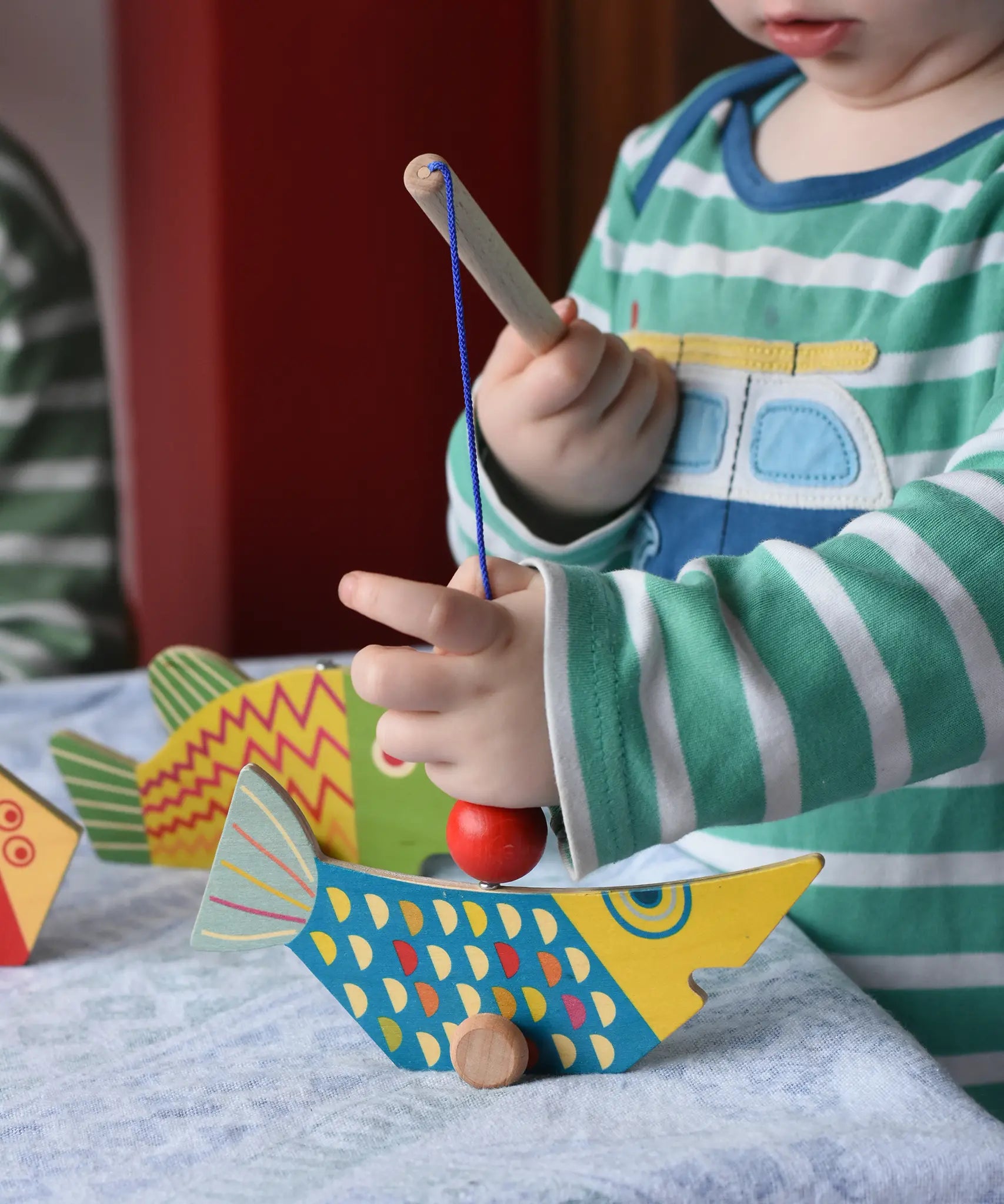 Bajo magnetic fishing game toy. Child holding wooden rod placing it onto blue fish.