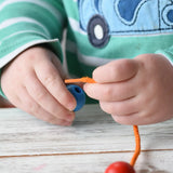 Close up of a child holding a threa nd bead from the Bajo Mathematical Threading Beads Game. The child is about to thread the lace through the blue bead.