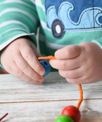 Close up of a child holding a threa nd bead from the Bajo Mathematical Threading Beads Game. The child is about to thread the lace through the blue bead.