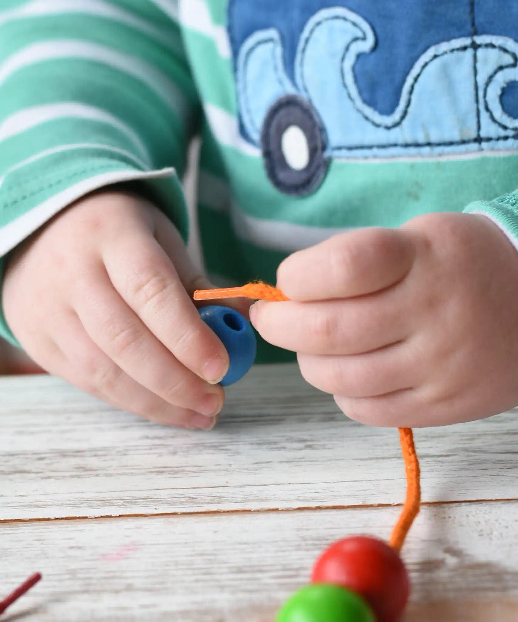 Close up of a child holding a threa nd bead from the Bajo Mathematical Threading Beads Game. The child is about to thread the lace through the blue bead.