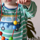 A child playing with the Bajo Mathematical Threading Beads Game. Child holding up the thread with some beads threaded on.