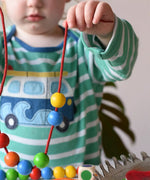 A child playing with the Bajo Mathematical Threading Beads Game. Child holding up the thread with some beads threaded on.