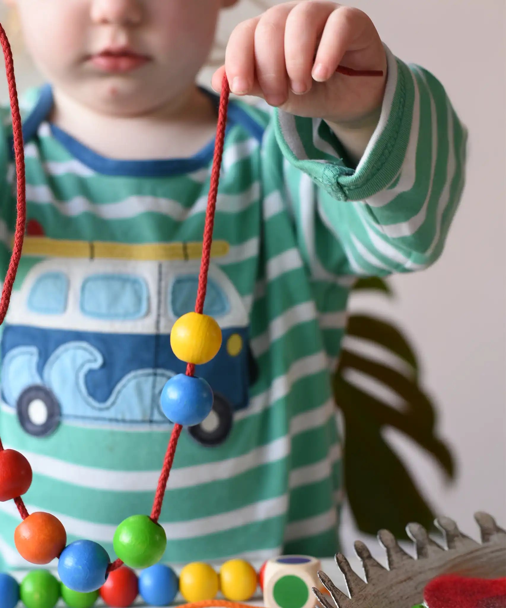 A child playing with the Bajo Mathematical Threading Beads Game. Child holding up the thread with some beads threaded on.