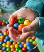 Close up of wooden beads from the Bajo Mathematical Threading Beads Game in a child's hand.