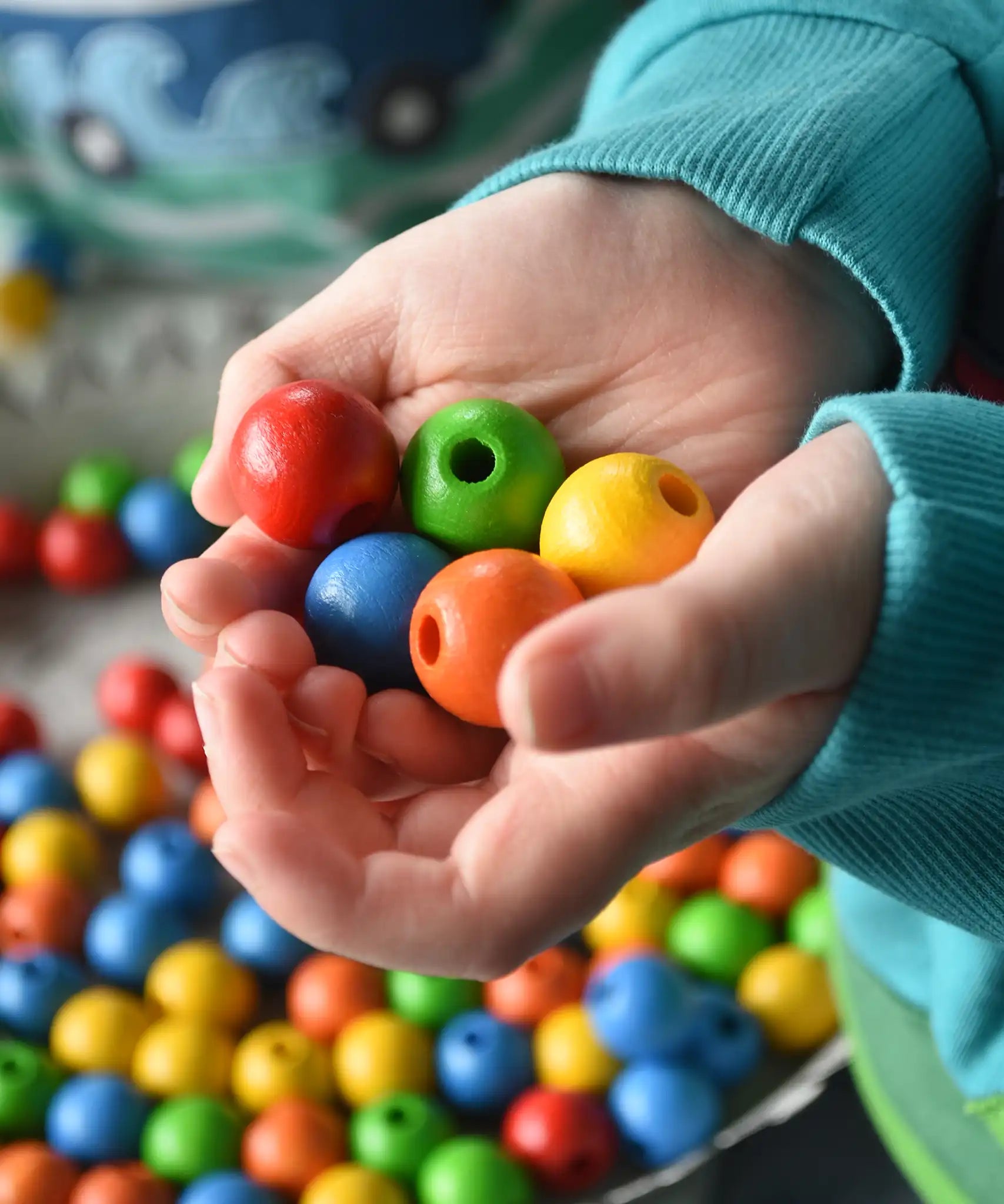 Close up of wooden beads from the Bajo Mathematical Threading Beads Game in a child's hand.