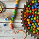 The contents of the Bajo Mathematical Threading Beads Game placed on a wooden surface. 