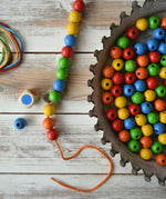 The contents of the Bajo Mathematical Threading Beads Game placed on a wooden surface. 
