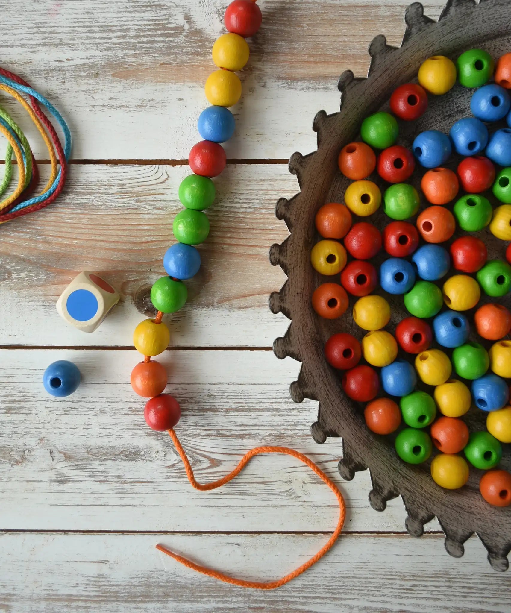 The contents of the Bajo Mathematical Threading Beads Game placed on a wooden surface. 