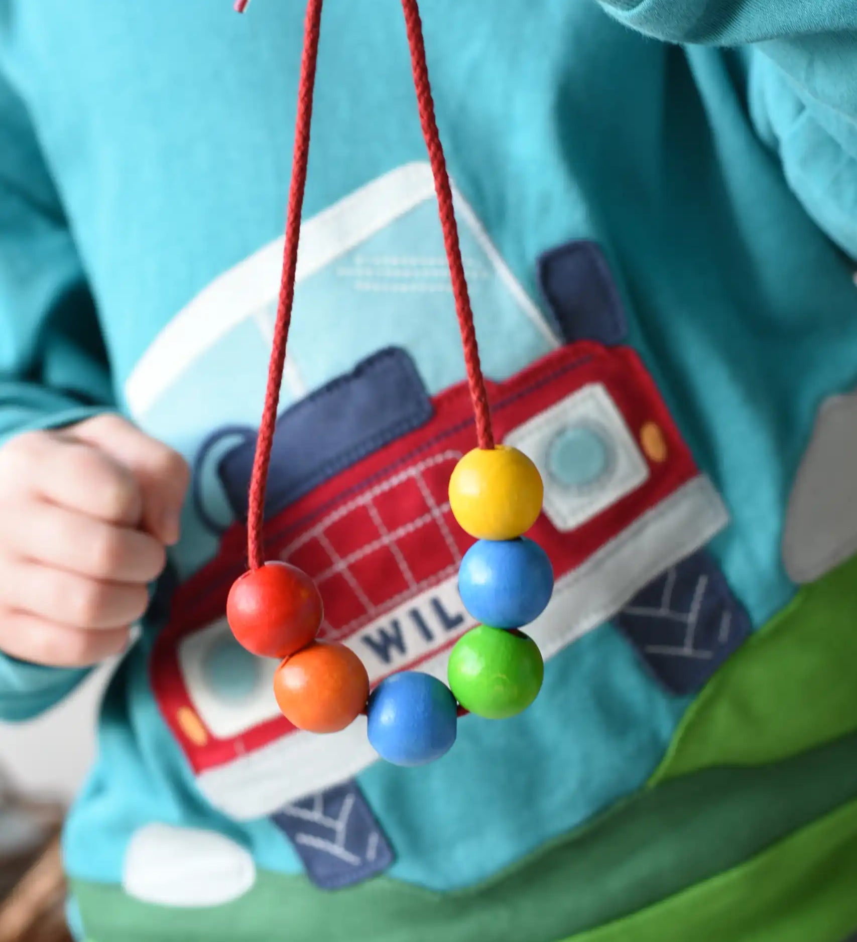 A child holding up a thread with 6 wooden beads on from the Bajo Mathematical Threading Beads Game.