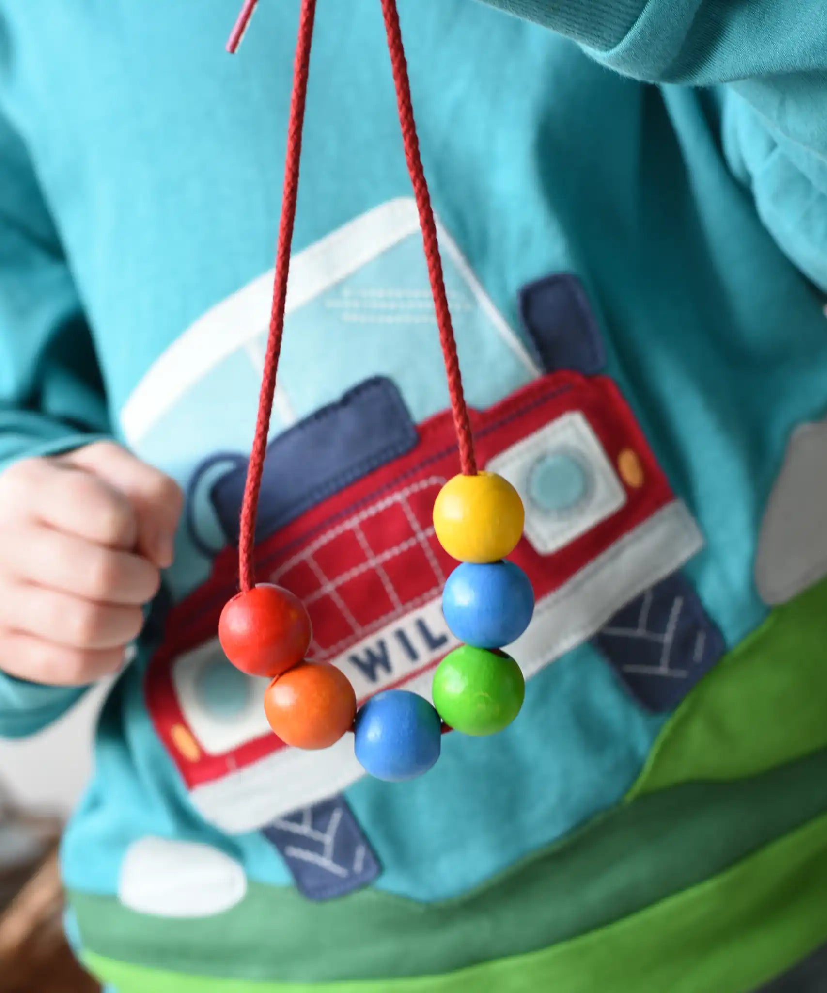 A child holding up a thread with 6 wooden beads on from the Bajo Mathematical Threading Beads Game.