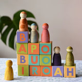 Bajo Me & You Alphabet Blocks with Grapat Wild crew wooden Nin peg dolls placed on top of them.