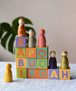 Bajo Me & You Alphabet Blocks with Grapat Wild crew wooden Nin peg dolls placed on top of them.