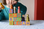 Child playing with the Bajo Me & You Alphabet Blocks. Blocks are stacked on top of each other and the child is placing the Grapat Nins Wild Crew peg dolls on top of them.