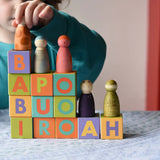 Child playing with the Bajo Me & You Alphabet Blocks. Blocks are stacked on top of each other and the child is placing the Grapat Nins Wild Crew peg dolls on top of them.