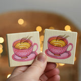An adult's hand holding up two tiles from the Bajo Wooden Tiles Memory Game. The tiles have an illustration of a pink dotty teacup on them. These heirloom quality toys by Bajo are part of a wide range of wooden toys available here at Babipur. 